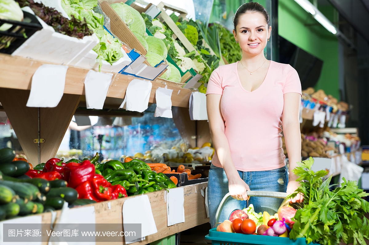 女人拿着篮子和新鲜的蔬菜,享受在蔬菜商店购买